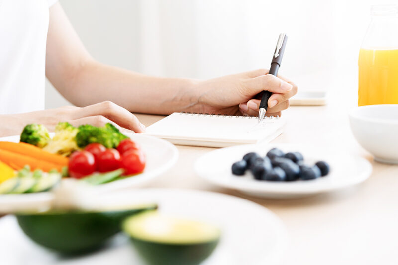 arm and hand on table writing in a notebook, fruit in bowls