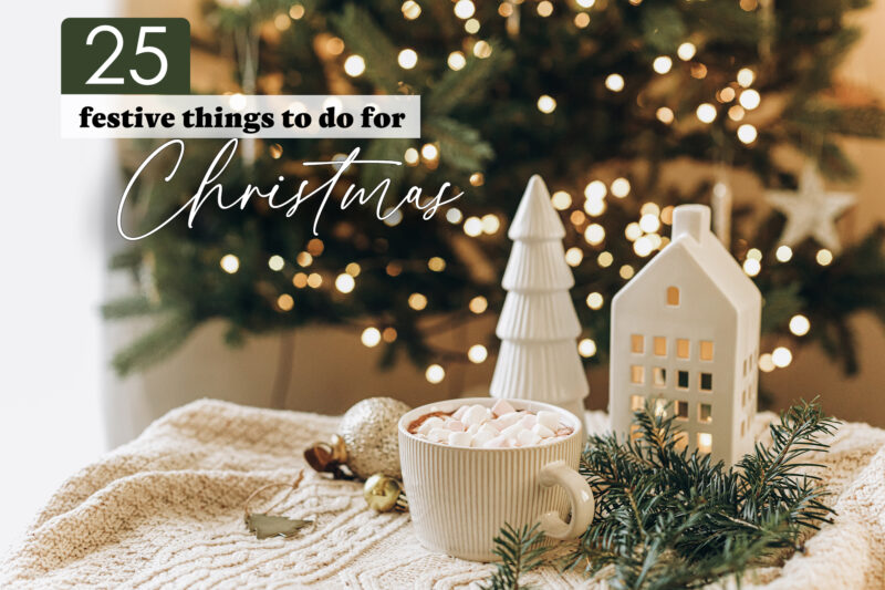 Christmas scene with a cup of hot chocolate, a tree, and house in front of a lit Christmas tree